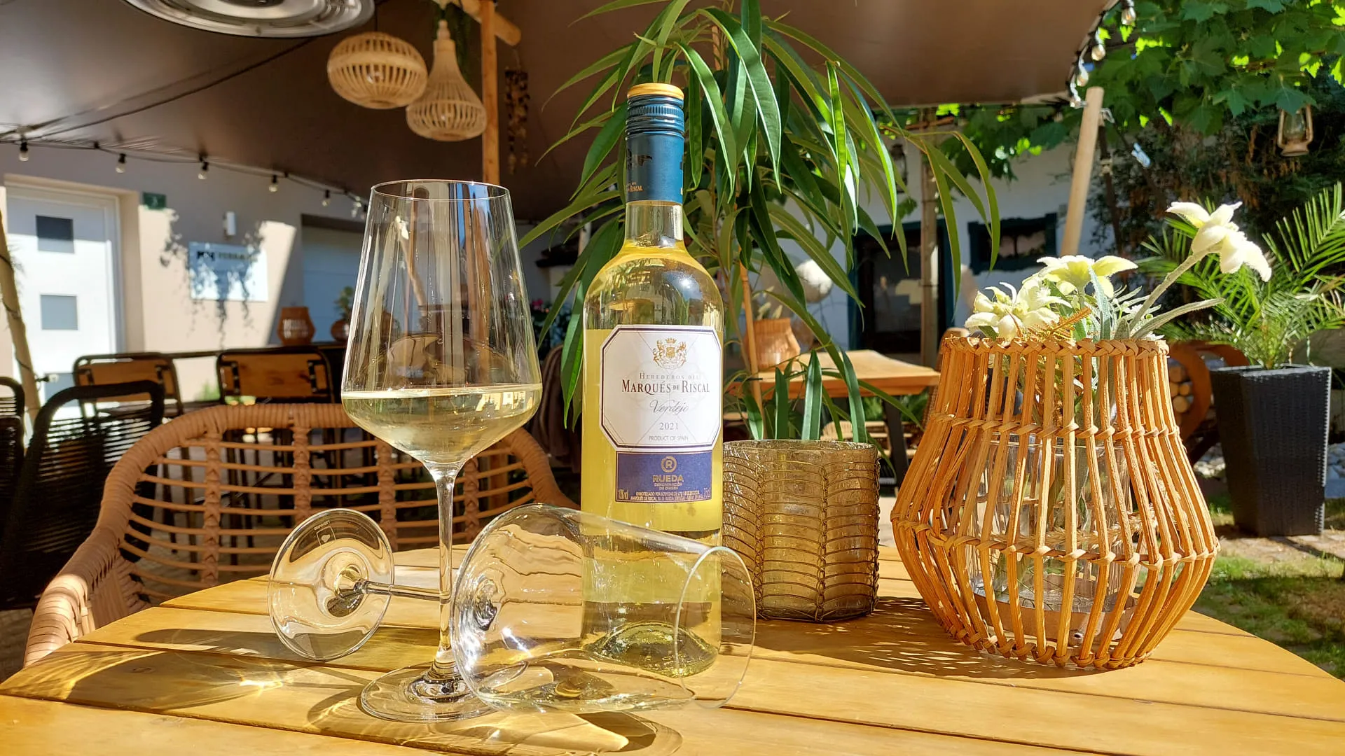 Weißweinflasche und Glas auf einem Tisch mit Pflanzen im Hintergrund