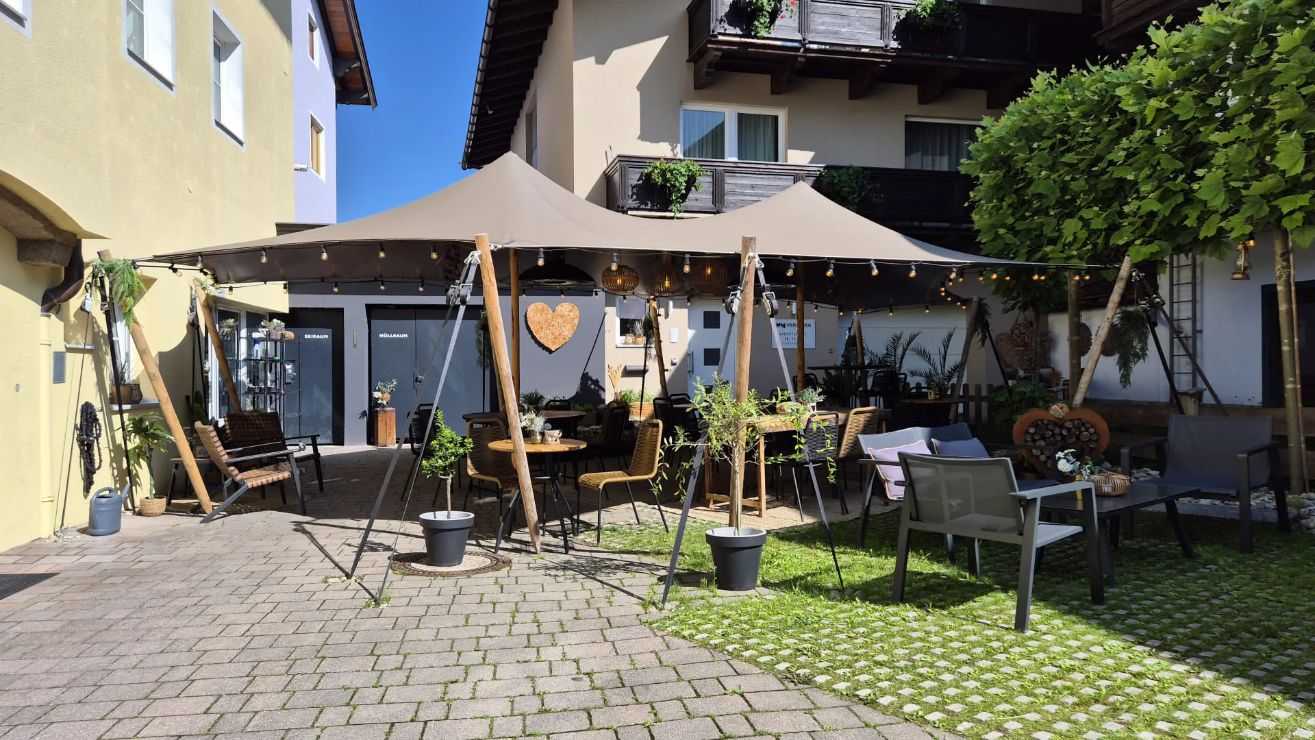 Ein Gartenbereich mit einem Zelt, Tischen und Pflanzen, umgeben von Gebäuden.