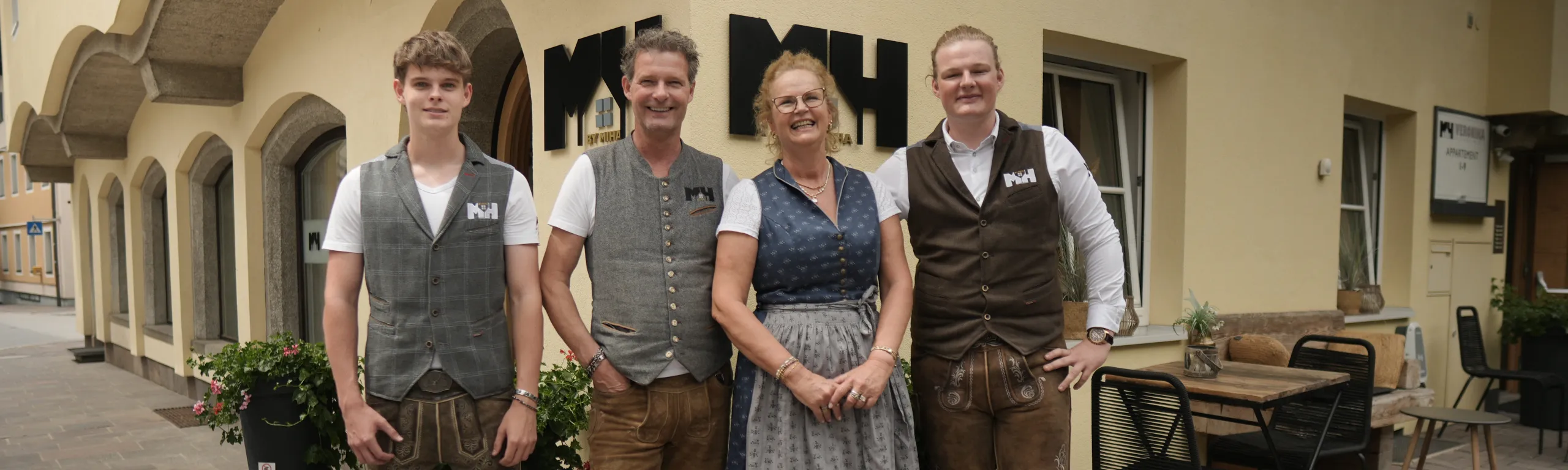 Familie vor einem Gebäude mit der Aufschrift 'Miha'.