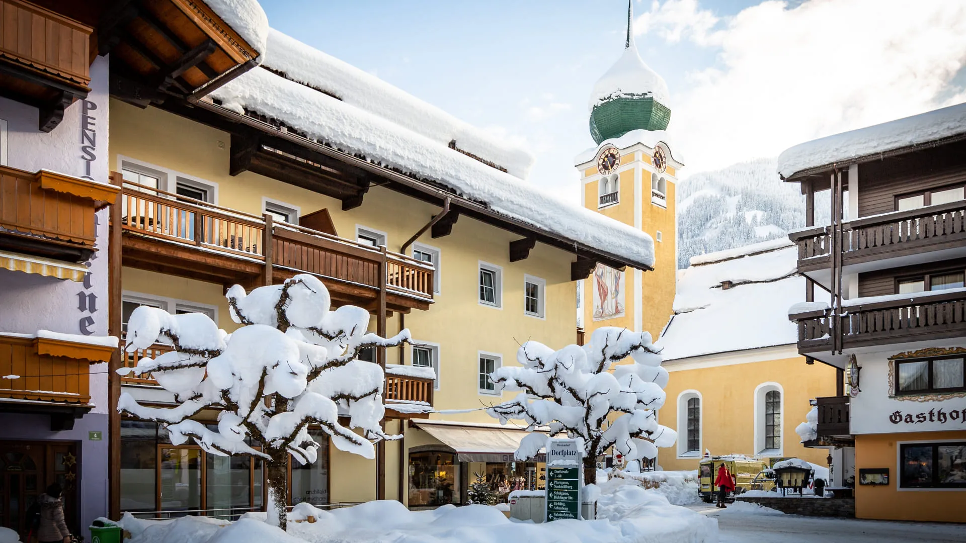 Winterliche Stadtansicht mit Schnee, hölzernen Balkonen und Uhrturm.